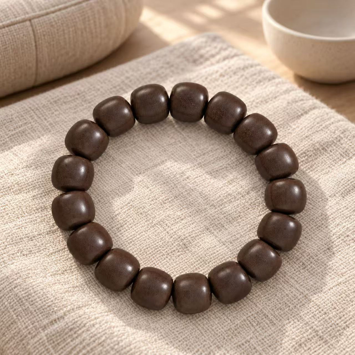 Dark brown wood bead bracelet arranged on light woven fabric beside a cup.