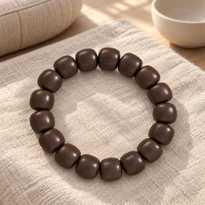 Dark brown wood bead bracelet arranged on light woven fabric beside a cup.